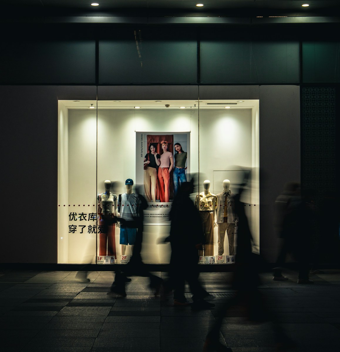 Photo by Li Lin People walk past a brightly lit storefront at night.